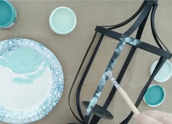 dry brushing blue-green paint onto a metal outdoor lantern for a faux patina finish.
