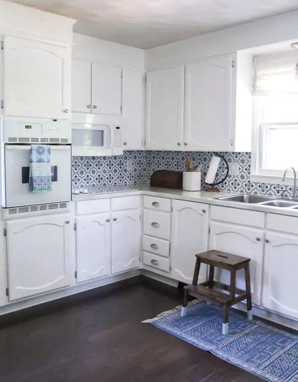 kitchen white cabinets painted white and a stenciled blue and white backsplash that looks like patterned tile.