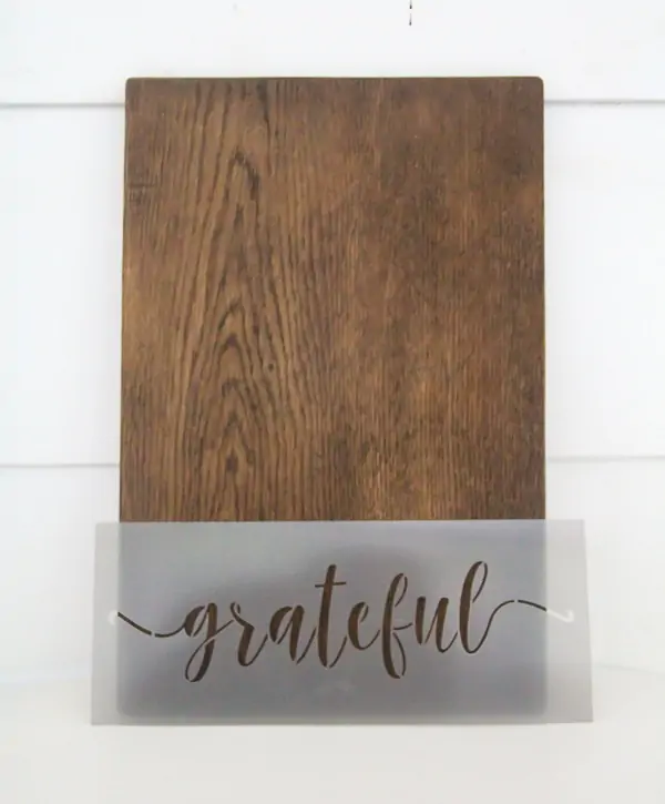plain wood cutting board next to stencil that says grateful.