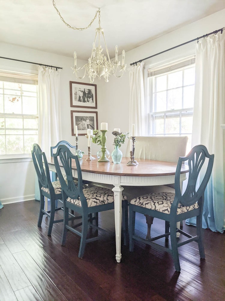 Dining room with traditional dining table with white legs and wooden top, blue dining chairs with gray and cream upholstery, and a gray leather settee.