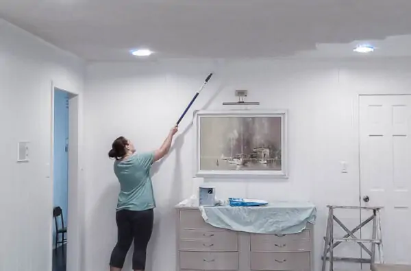 painting the ceiling using a paint roller extension pole.