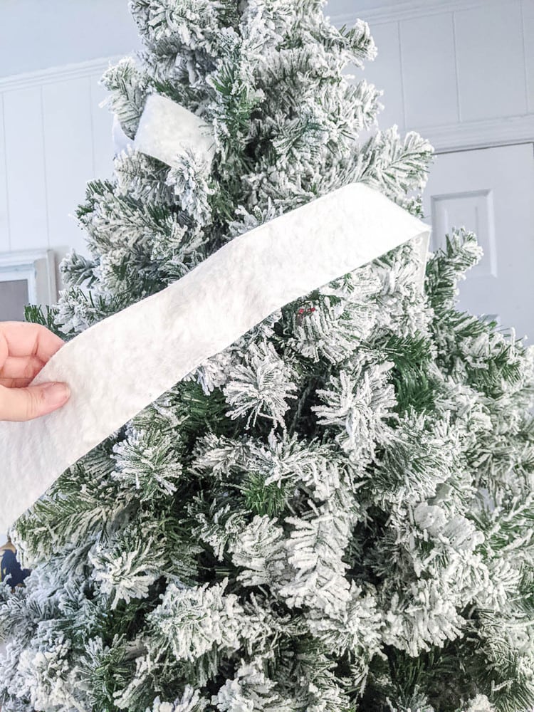 hand holding a piece of white ribbon with one end tucked into the Christmas tree.