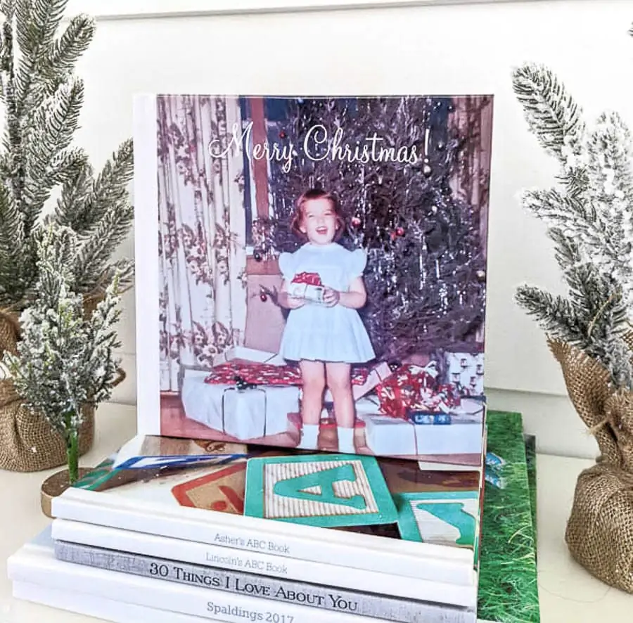 Christmas photo book on top of a stack of other photo books next to some mini Christmas trees.