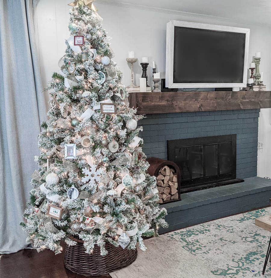 Decorated Christmas tree next to blue brick fireplace with wood mantel.