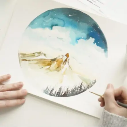 hands holding a paintbrush, painting a watercolor scene of a mountain.