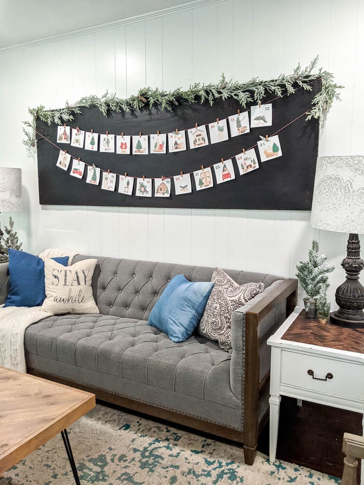 printable advent calendar hanging with bakers twine and mini clothespins over the couch with an evergreen garland.