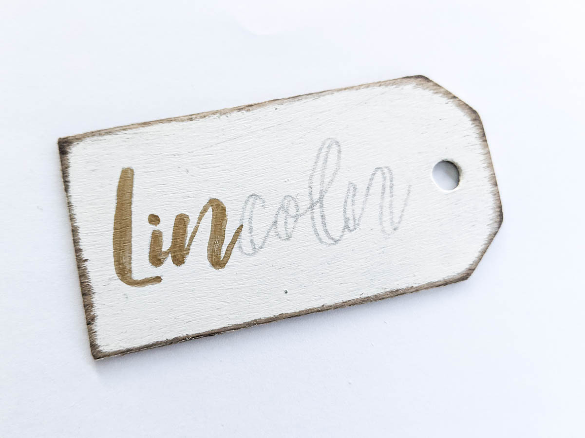 DIY stocking name tag with name half written with a gold paint marker.