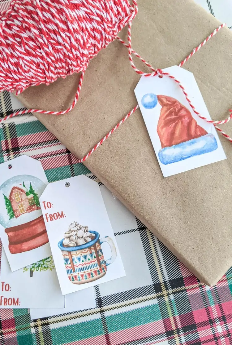 Gift wrapped with brown butcher paper and red and white baker's twine with a gift tag with a watercolor Santa hat.