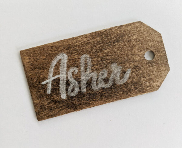 Stained wood name tag with faded, messy white writing.