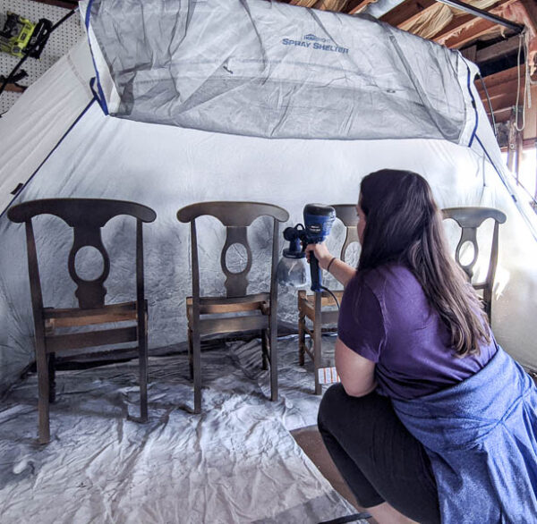 painting wooden chairs in spray tent with a paint sprayer.