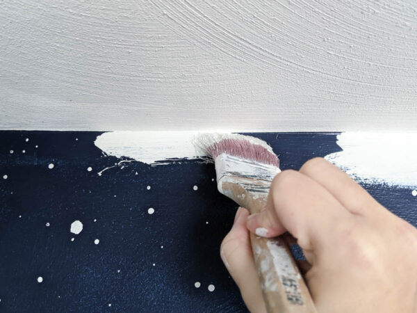 using a paint brush to cut in around the edge of the wall next to the ceiling.