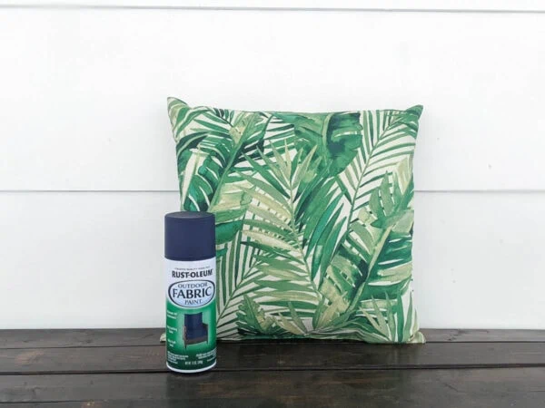 outdoor pillow with a green leaf pattern next to a can of Rustoleum outdoor fabric paint.