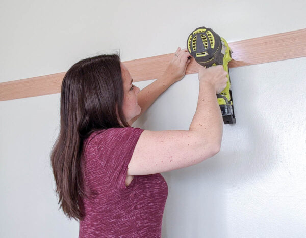 using a nail gun to attach the first wood plank to the wall.