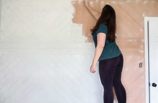 Painting a wood plank wall with a paint roller.