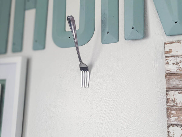 a fork on the wall with a nail between two of the tines.