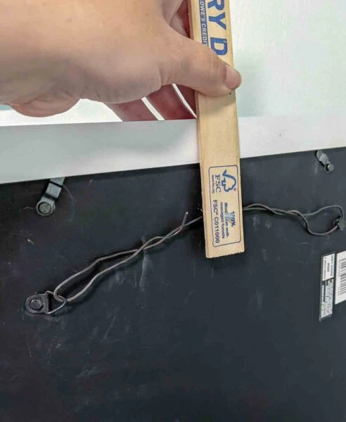 holding frame up with paint stick and screw tool.