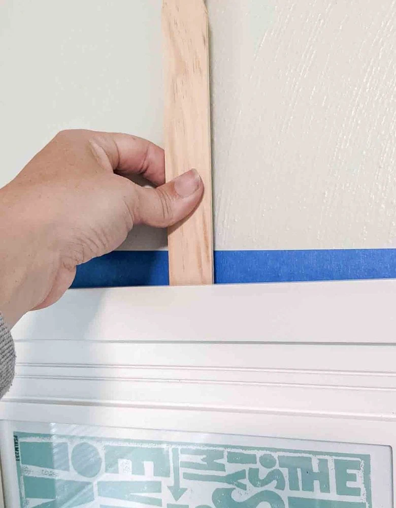 holding frame on wall by paint stick with screw tool.