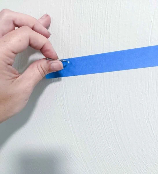 preparing to hammer nail through hole in painter's tape on wall.