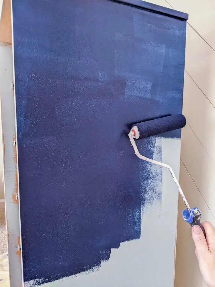 using a small foam roller to roll navy blue paint over baby blue paint on furniture.
