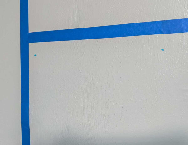 two dots of toothpaste on wall next to a strip of painter's tape.