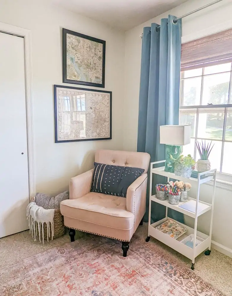 Corner of office with armchair next to a utility cart with pens and materials and a basket holding a blanket and pillow.