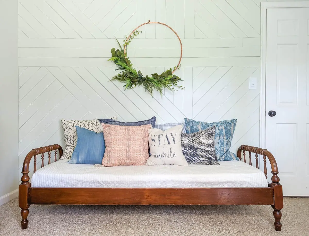 antique wooden daybed in front of geometric wood wall painted white.