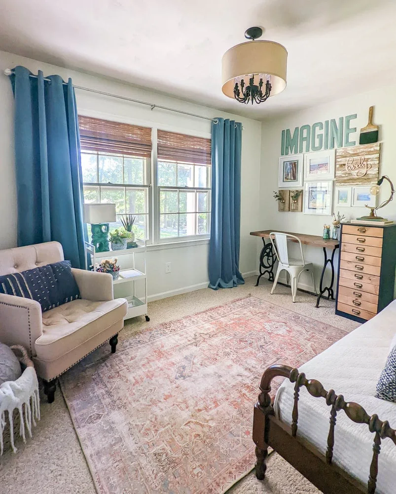 Home office with upcycled wood desk, chest of drawers, weathered rug, beige armchair, and teal velvet curtains.