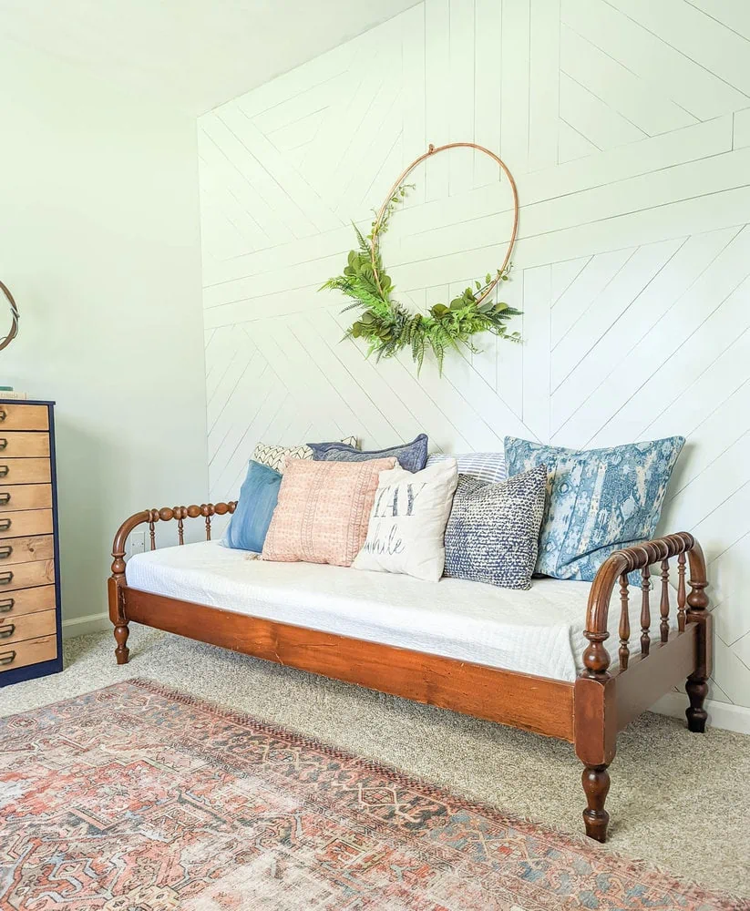 Antique wood daybed in front of white wood accent wall with big copper wreath.