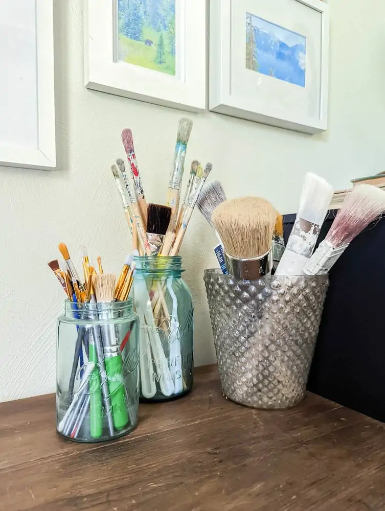 paintbrushes stored in two old mason jars and a mercury glass vase.