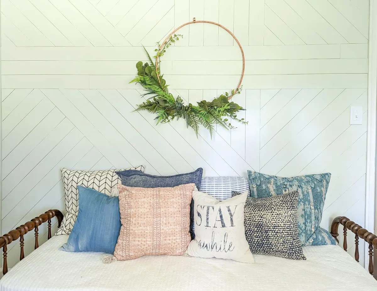 wooden daybed with cream quilt and a pile of pillows in various colors and prints.