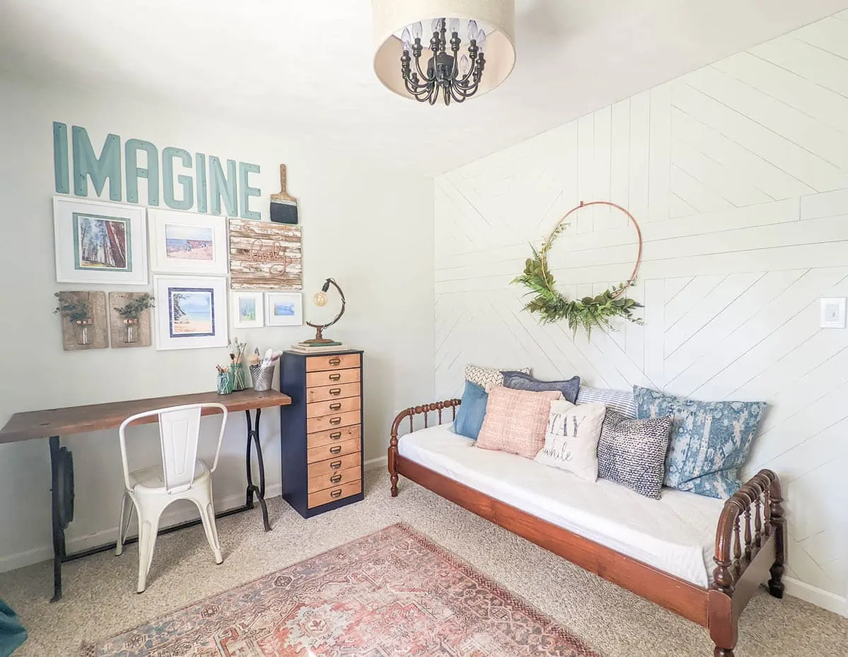 view of two walls of office with wood wall and daybed on one wall and upcycled desk, chest of drawers and gallery wall on the adjoining wall.