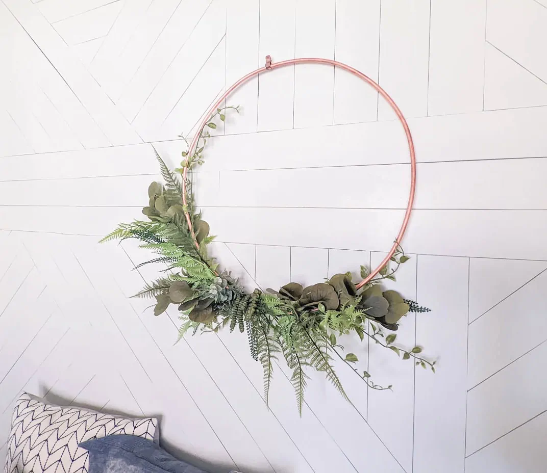 copper wreath against white wood accent wall.