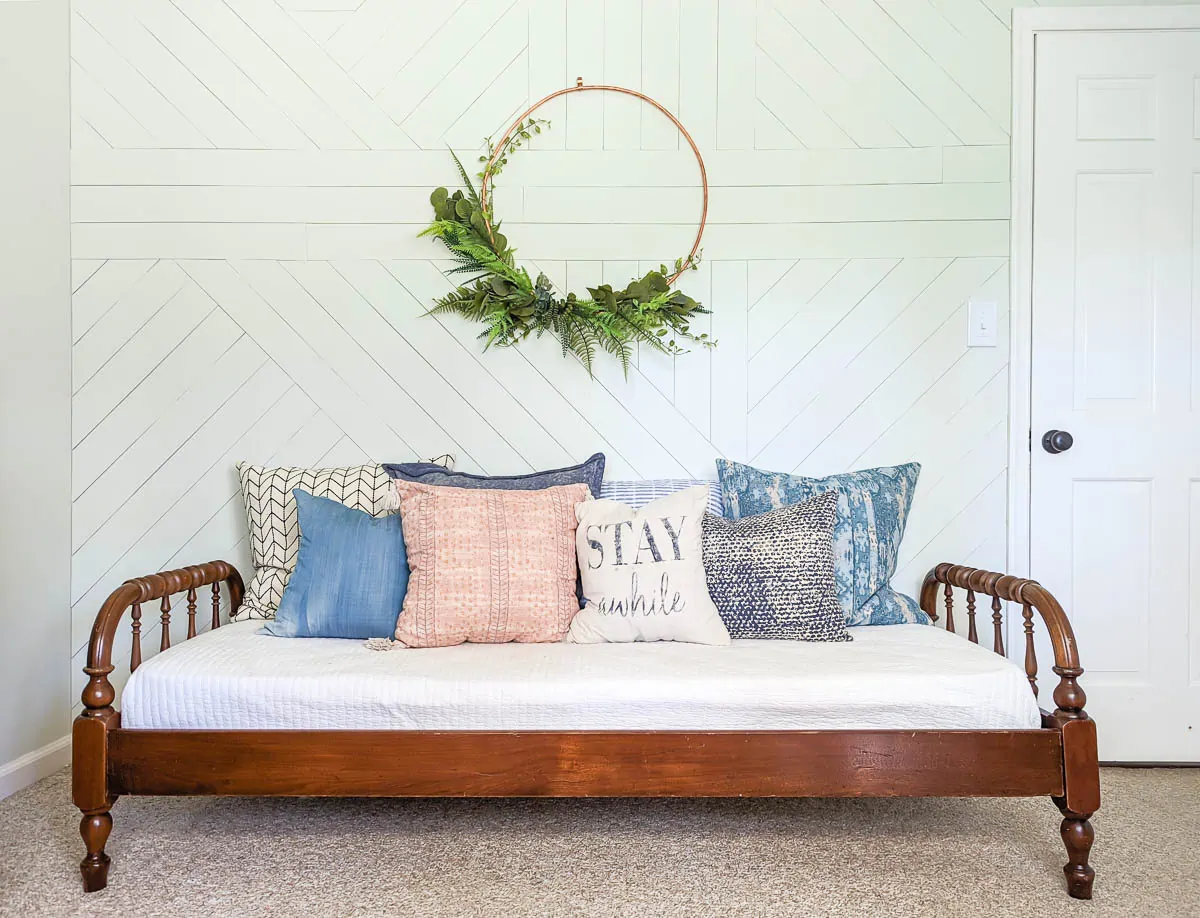 large copper wreath on white wood wall above wooden daybed.