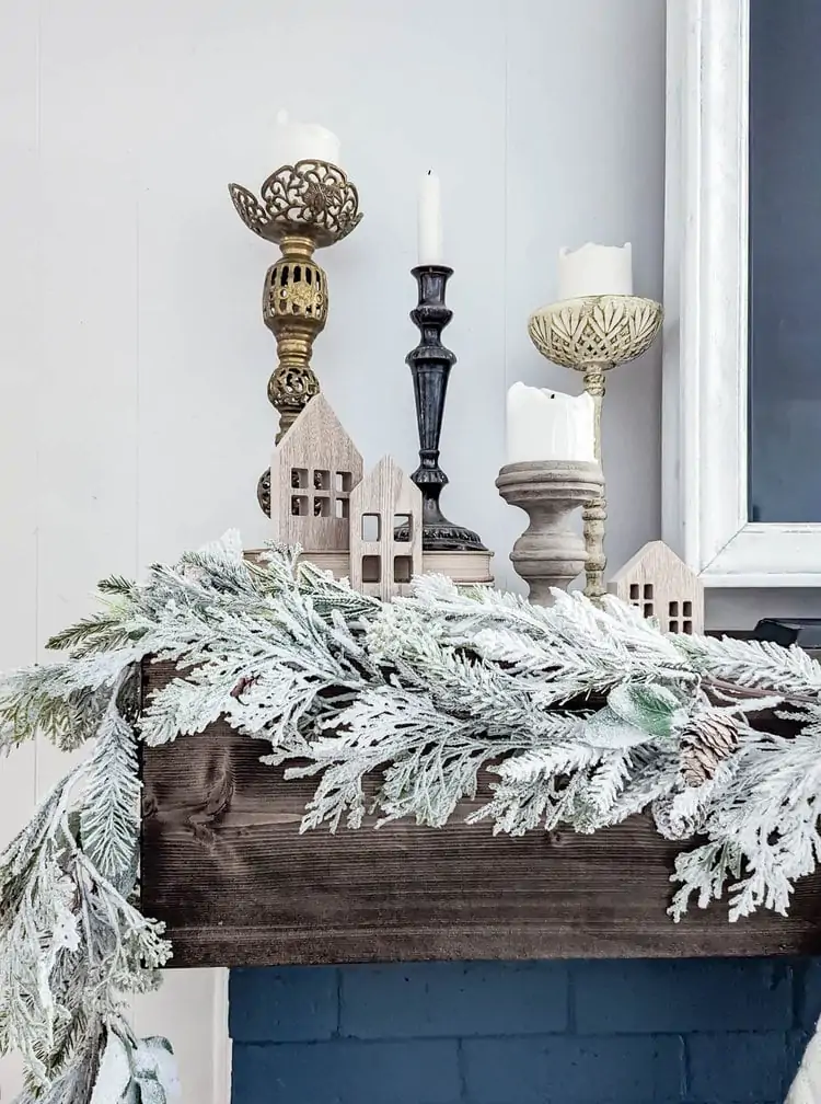 vintage candlesticks and small wooden houses next to TV on Christmas mantel.