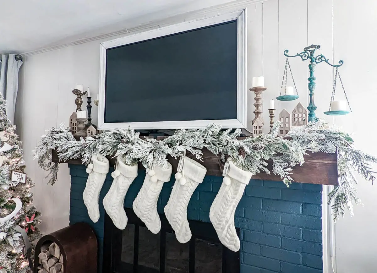 Christmas mantel with flocked garland, white stockings, and candlesticks around TV.