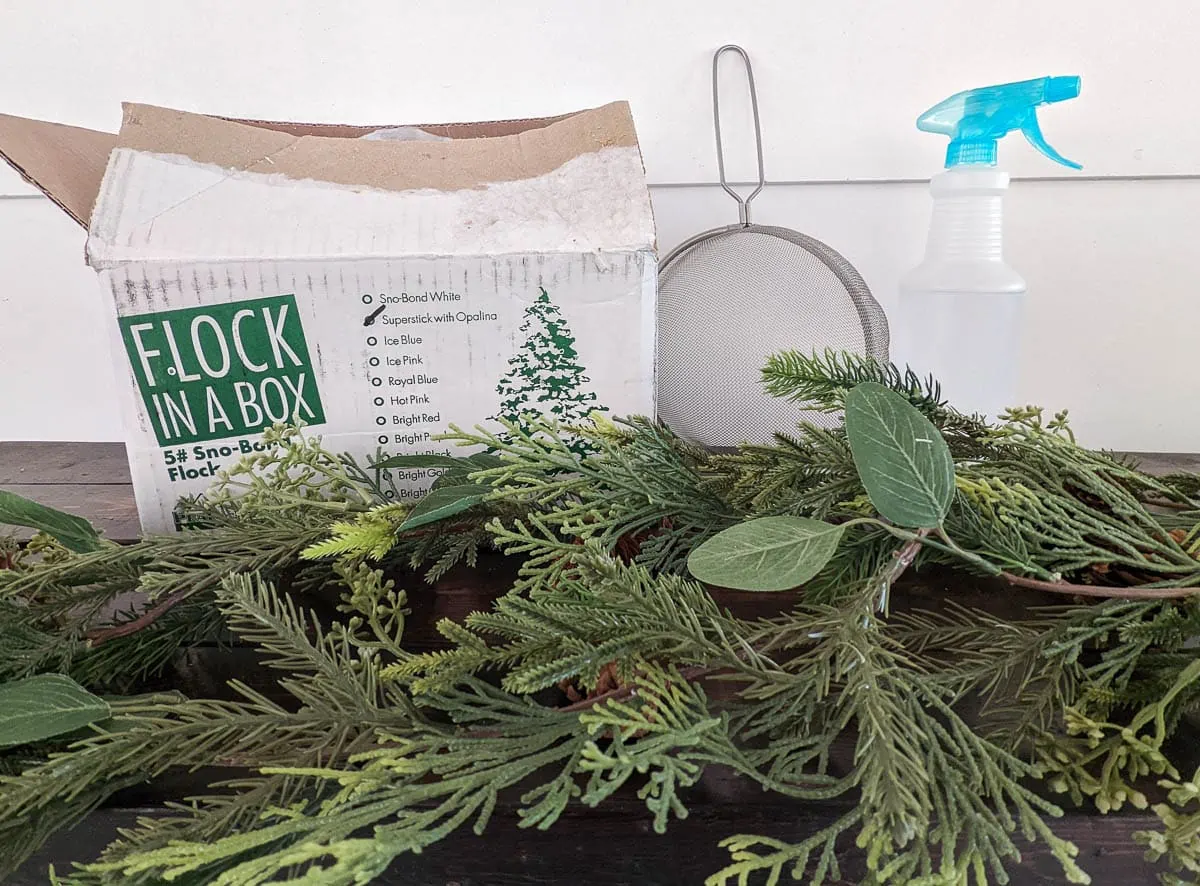 materials for flocking garland - box of snow flocking powder, spray bottle of water, strainer, green garland.