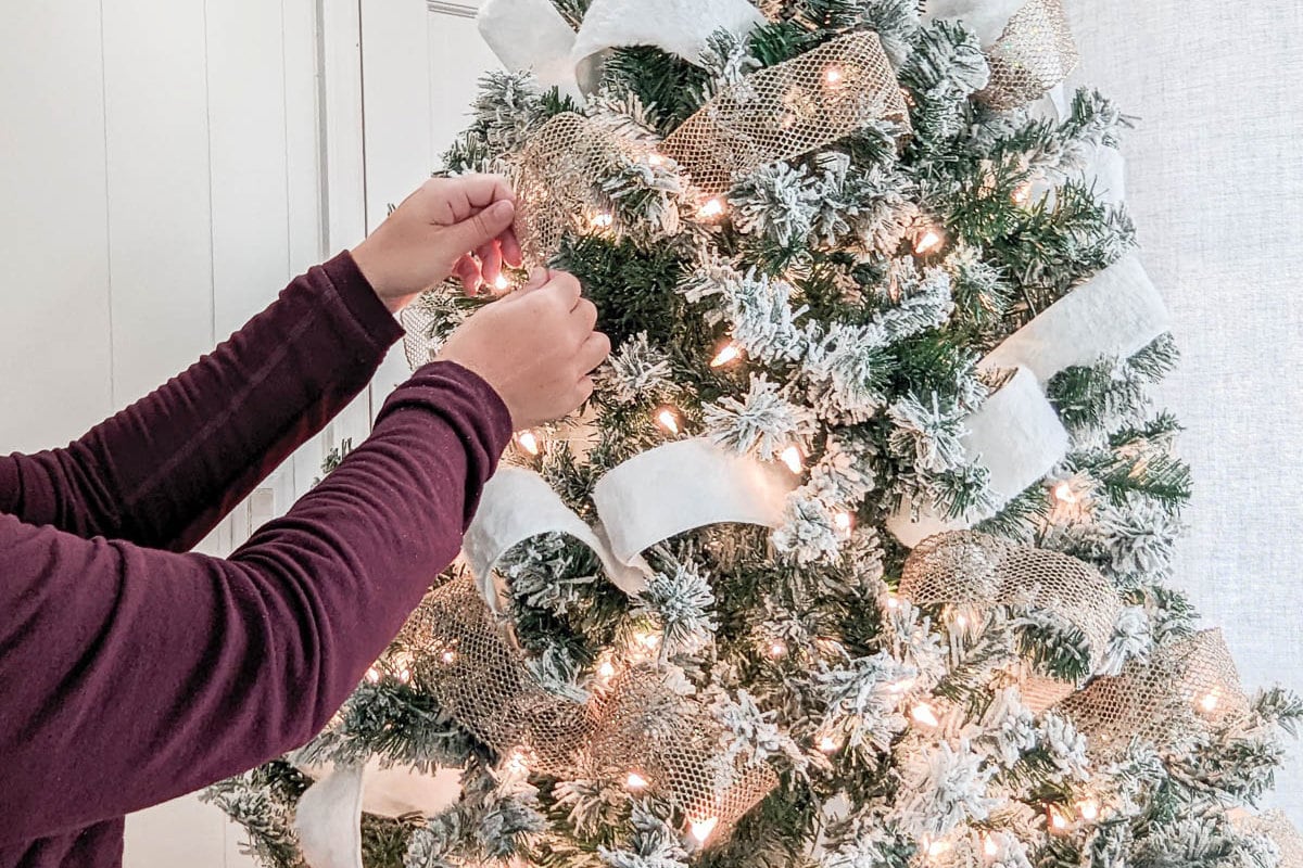 two hands adjusting ribbon on Christmas tree.