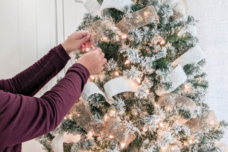 hands putting ribbon on Christmas tree.