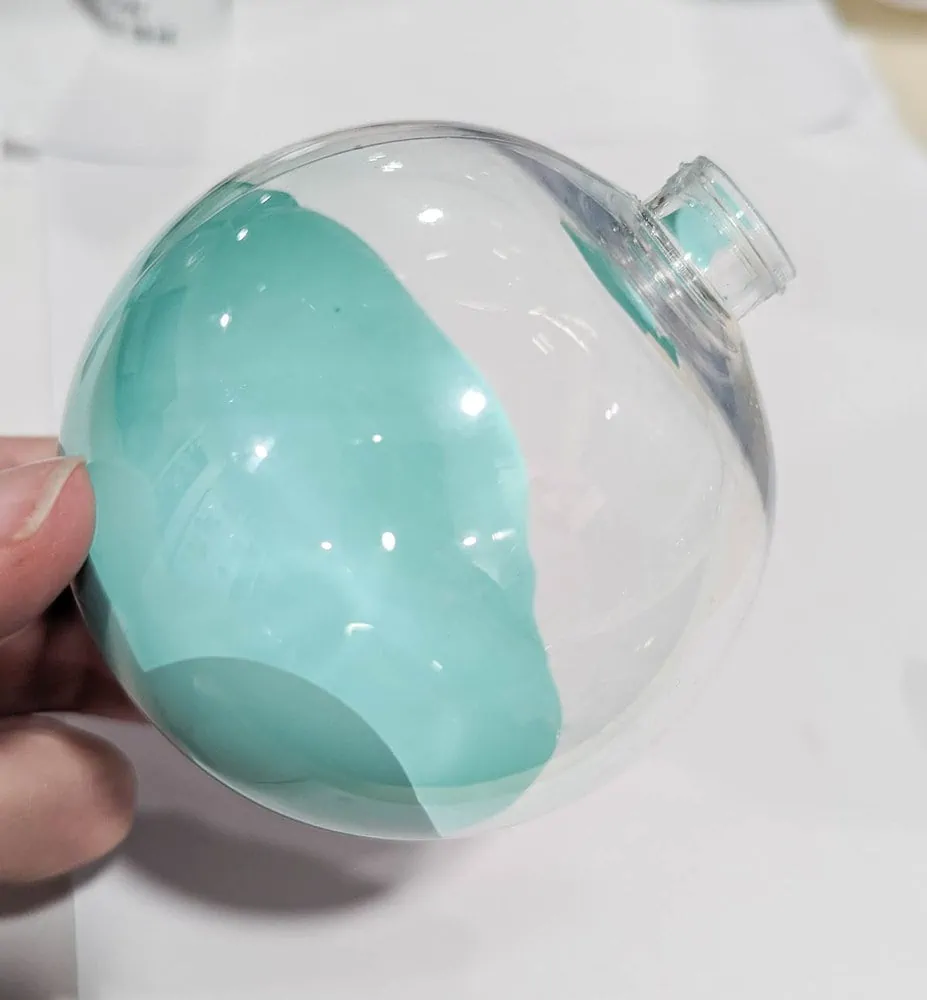 filling a clear ornament with aqua paint.