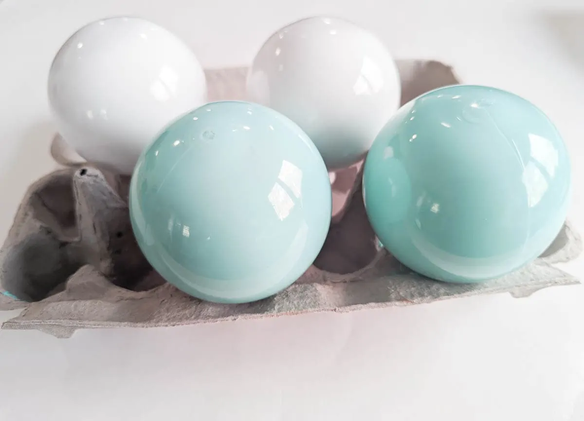 clear ball ornaments filled with blue and white paint, drying on an egg carton.