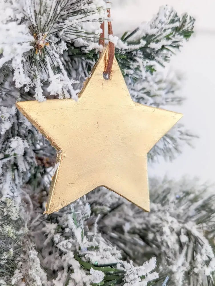 star ornament covered in gold leaf hanging on Christmas tree.