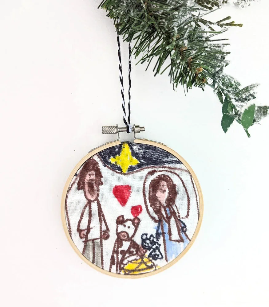 embroidery hoop ornament with child's drawing of nativity against white background.