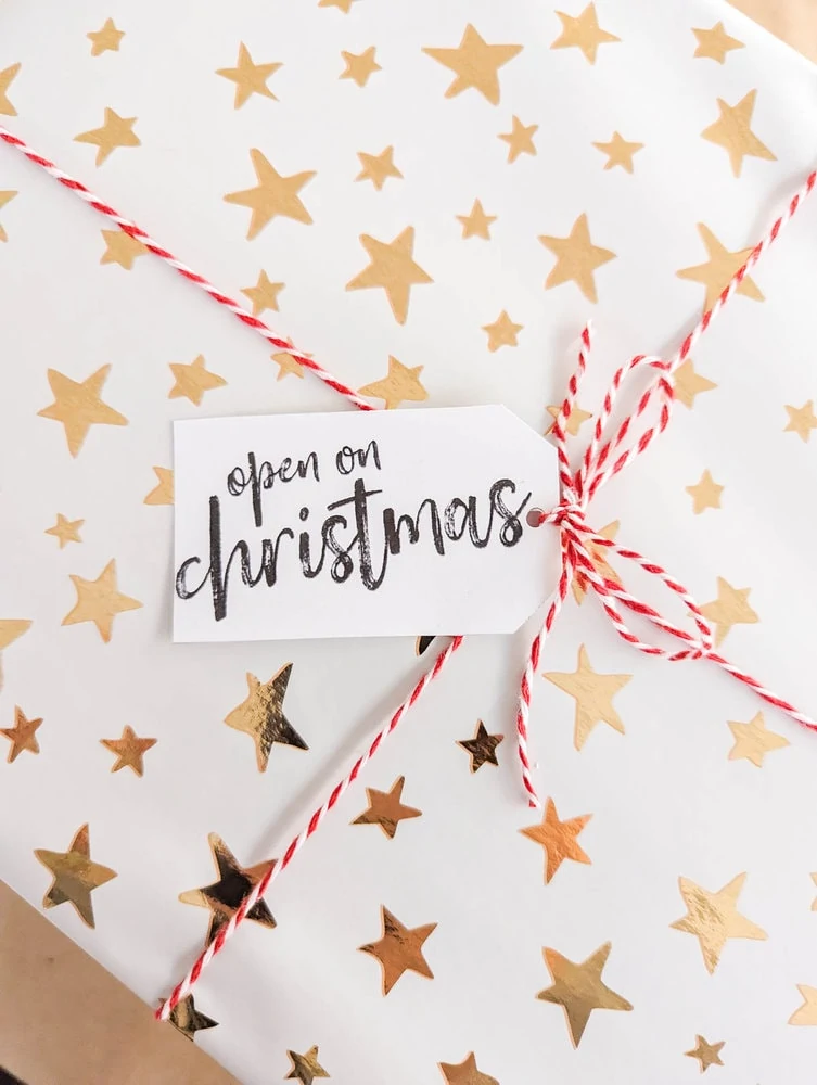 present wrapping in white wrapping paper with gold stars, tied with red and white twine with gift tag that says open on christmas.