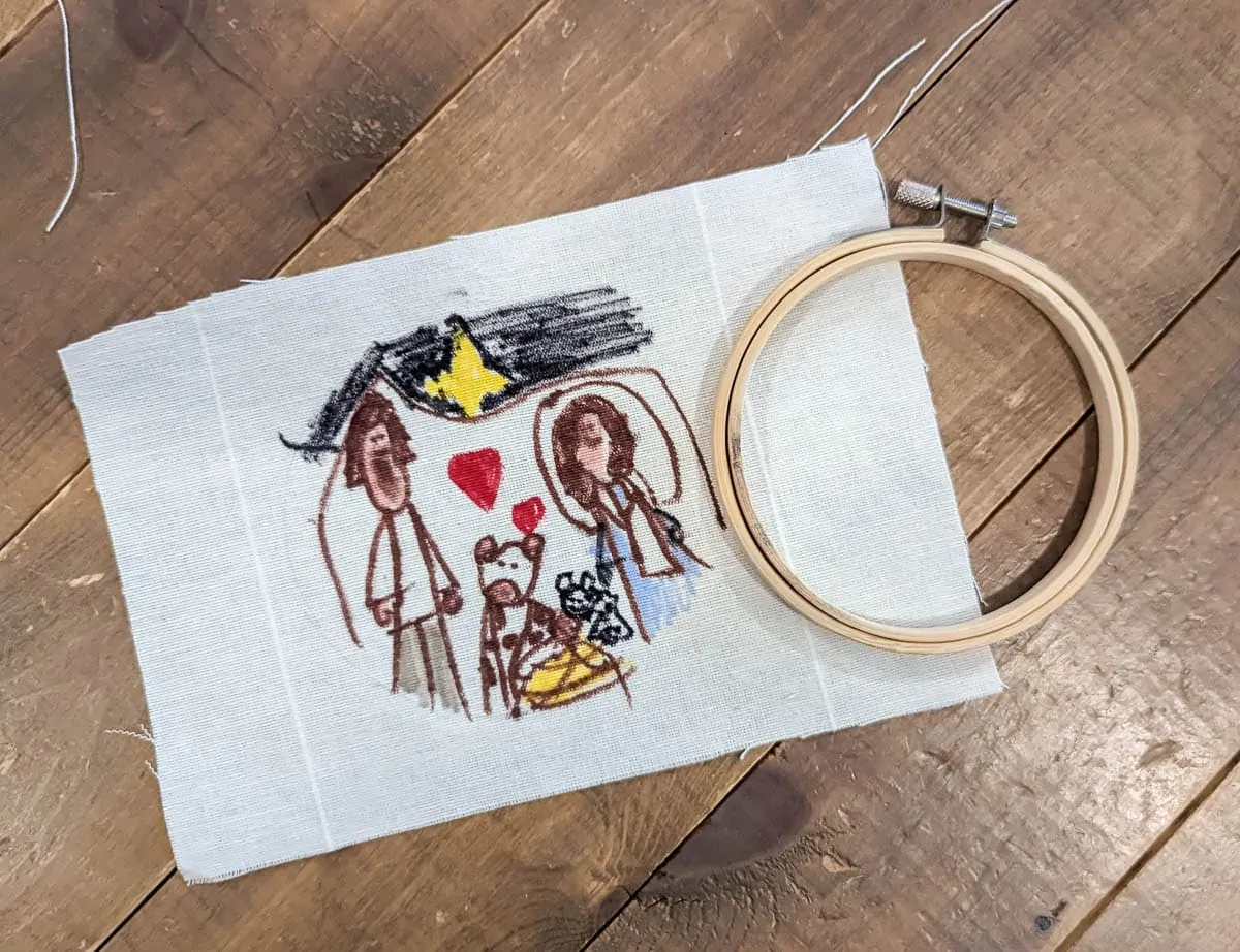 child's drawing of the nativity on fabric next to a small embroidery hoop.