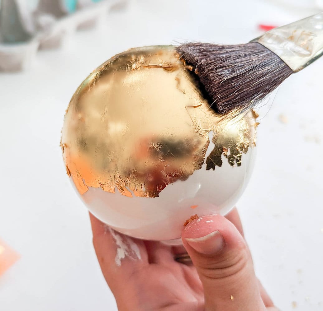 smoothing gold leaf onto ball ornament using paint brush.