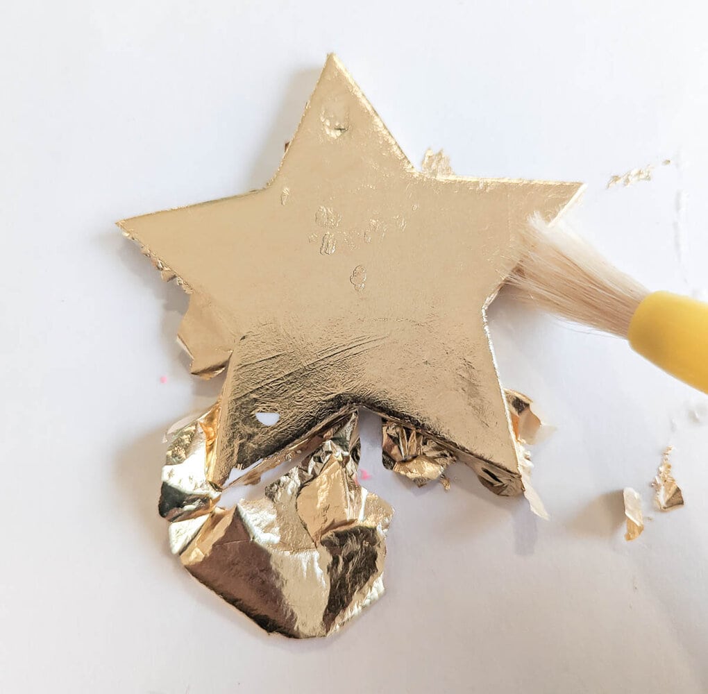 smoothing gold leaf onto star ornament using paint brush.
