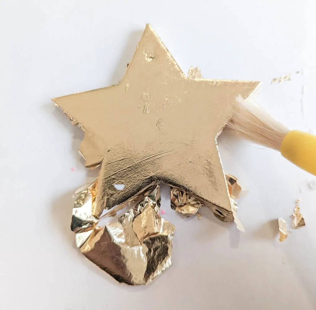 smoothing gold leaf onto star ornament using paint brush.