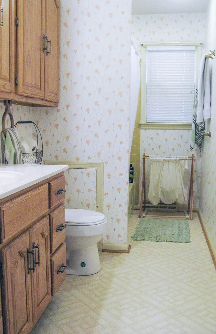 bathroom with floral wallpaper, vinyl flooring, and dated cabinets.
