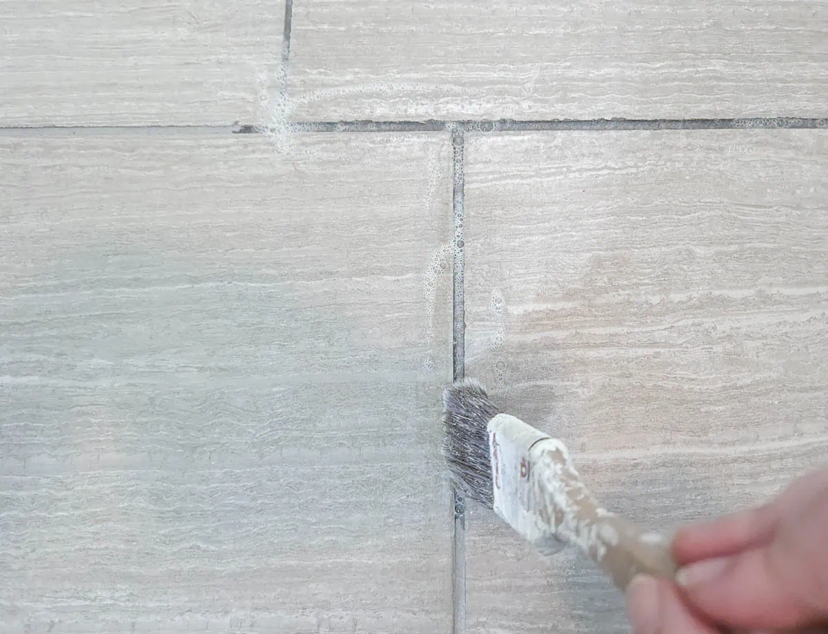 brushing on grout sealer with a paint brush.