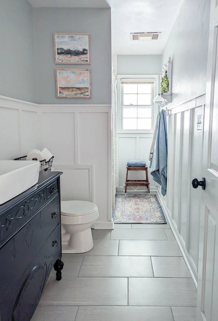 budget bathroom makeover with gray walls over board and batten, a navy painted vanity, and updated art.